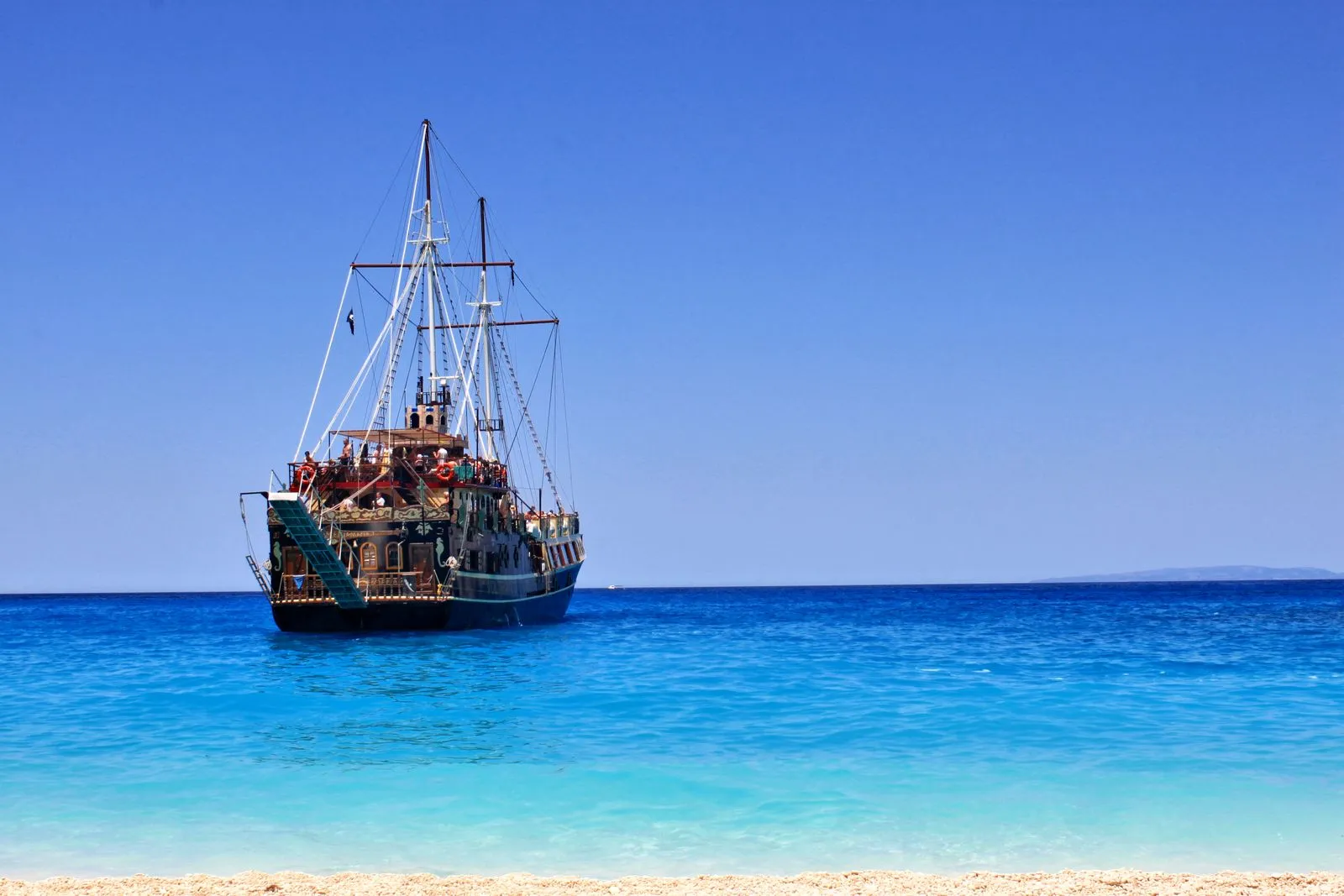 Navio pirata de madeira ancorado em mar azul-turquesa junto à praia